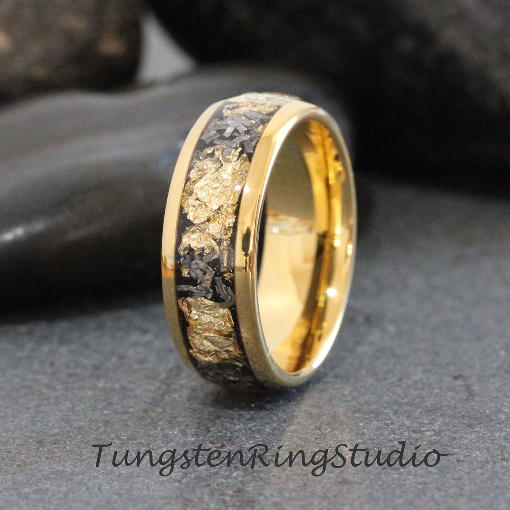 May include: A gold tungsten carbide ring with a black inlay featuring gold flecks. The ring has a polished finish.