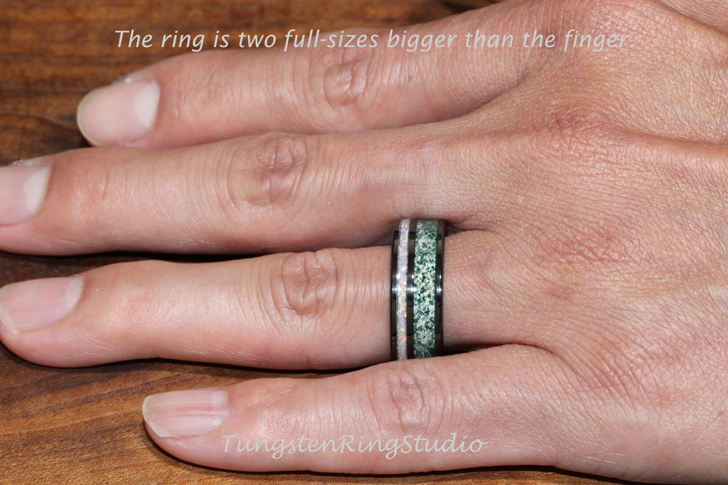 May include: A black tungsten ring with a green and white inlay. The ring is worn on a finger.
