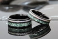 May include: Two black tungsten carbide rings with green and white inlay. The rings are stacked on top of each other.
