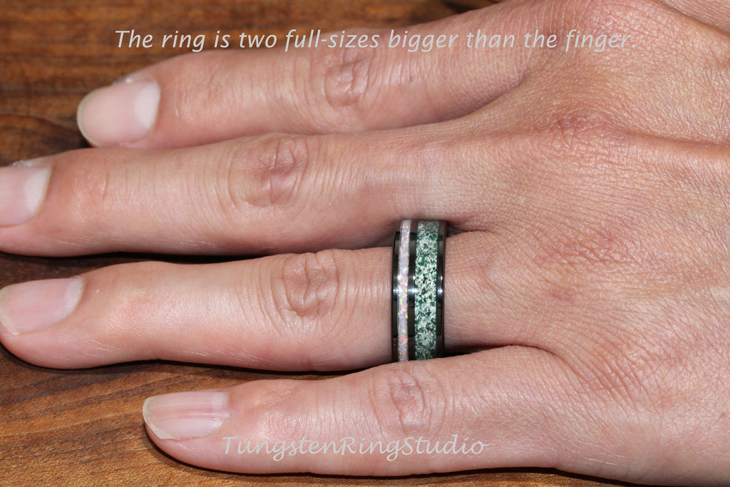 May include: A black tungsten ring with a green and white inlay. The ring is worn on a finger.
