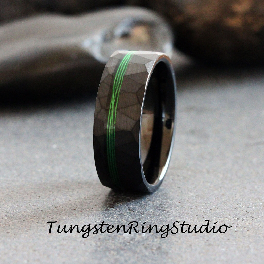 May include: Black tungsten carbide ring with a hammered finish and green inlay. Tungsten Ring Studio.