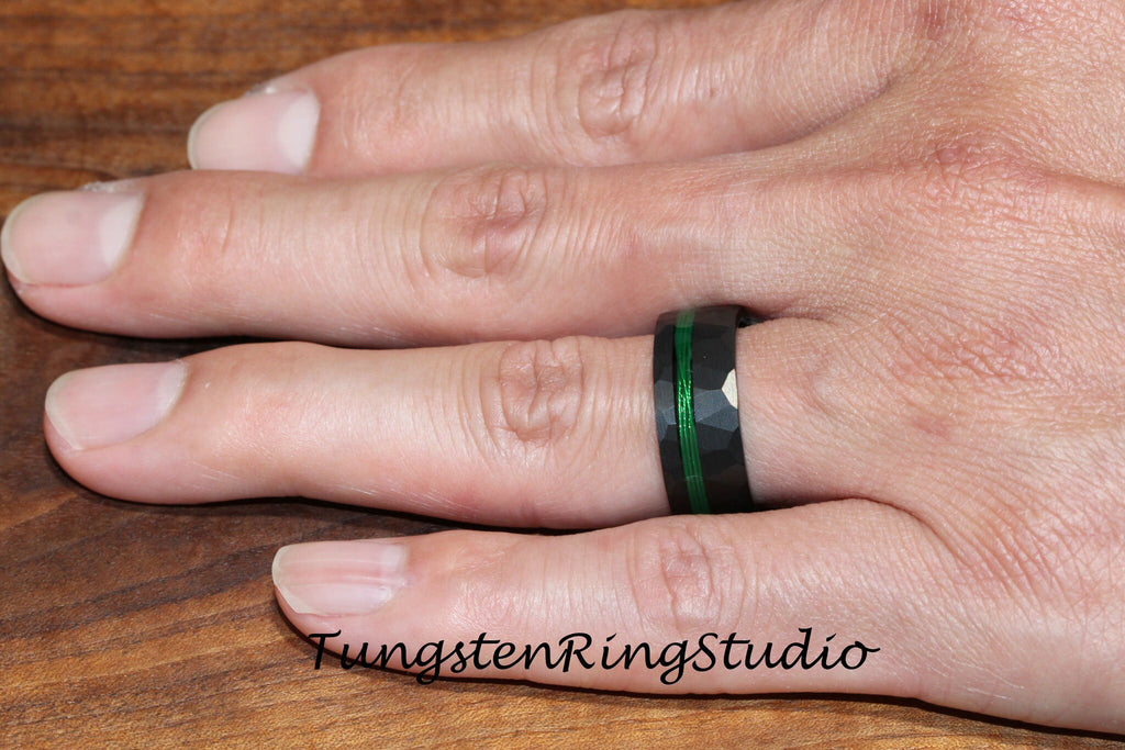 May include: A black tungsten ring with a green inlay and a hammered finish. The ring is worn on a person's finger.