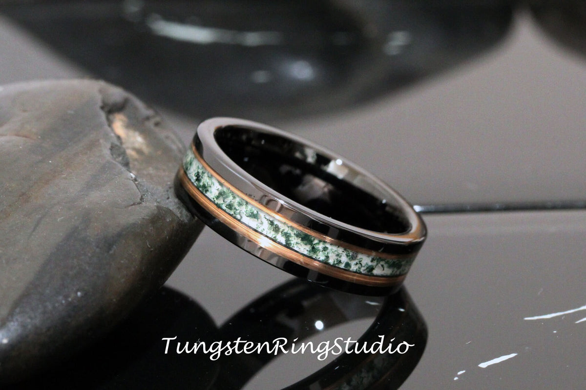 May include: A tungsten ring with a black and silver band and a green and copper inlay. The ring is on a gray stone surface.