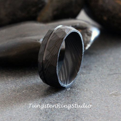 May include: A black tungsten carbide ring with a hammered finish and a polished groove. The ring has a unique, textured pattern.