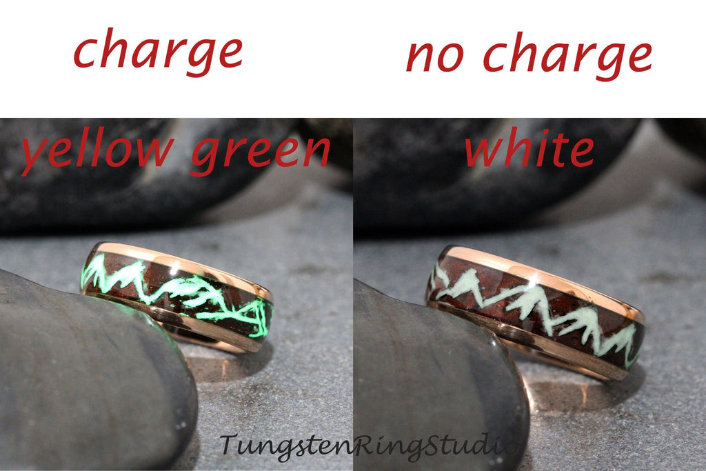 May include: A tungsten ring with a dark brown wood inlay and a glow-in-the-dark mountain design. The ring is shown in two states: charged, glowing green, and uncharged, with a white glow. The text "charge" and "no charge" is shown above the rings, and the text "yellow green" and "white" is shown below the rings.