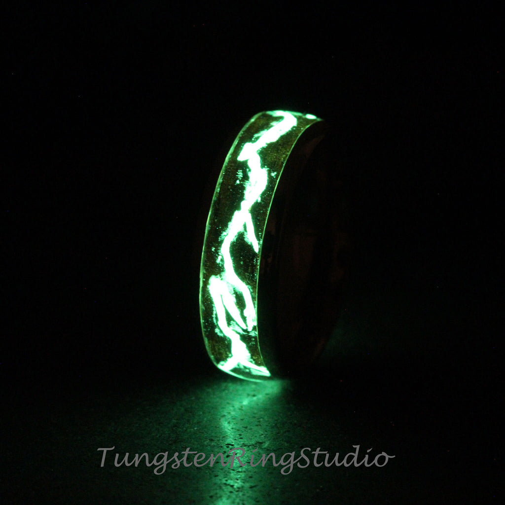 May include: A black tungsten ring with a green glow-in-the-dark inlay. The inlay is a swirling pattern of lines.