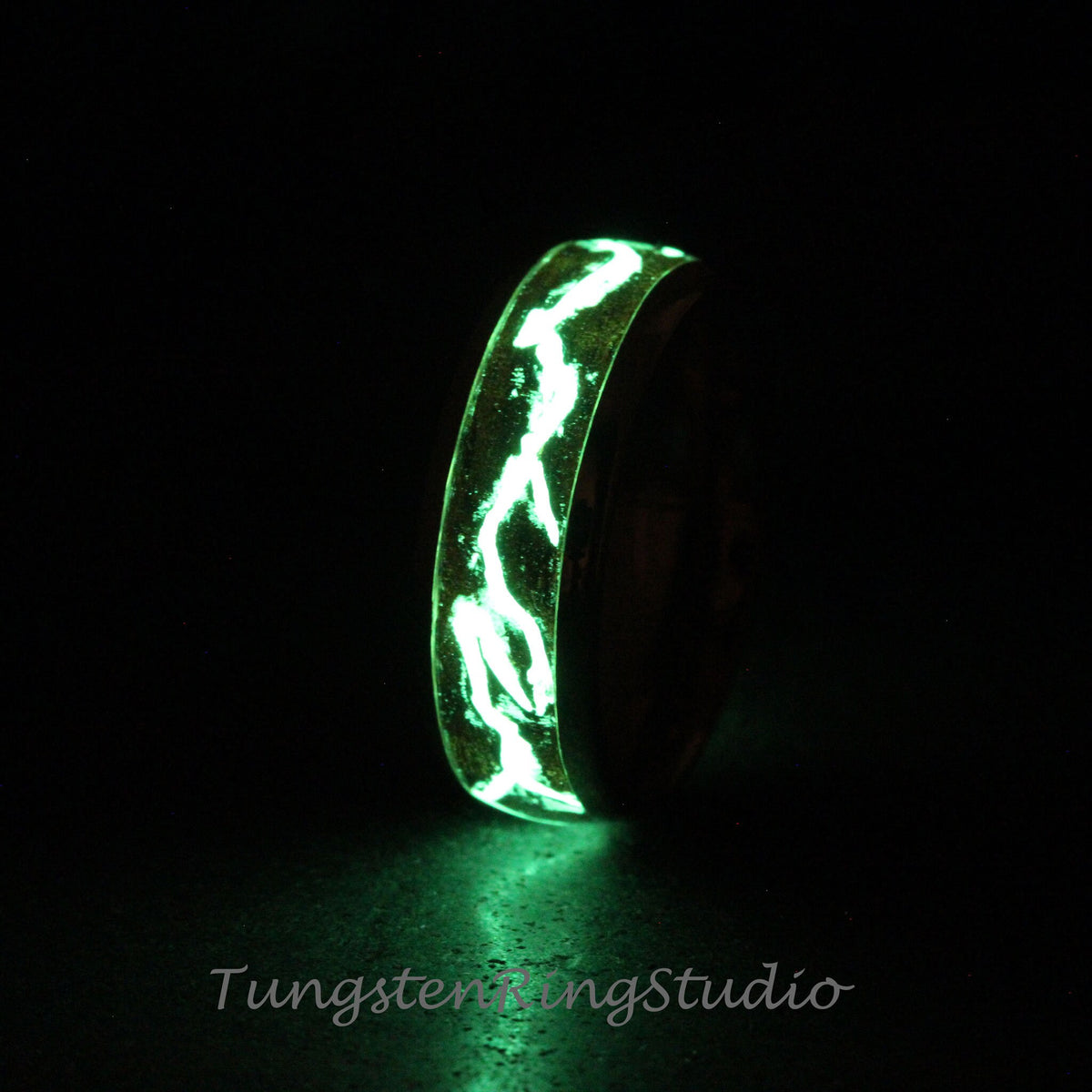 May include: A black tungsten ring with a green glow-in-the-dark inlay. The inlay is a swirling pattern of lines.