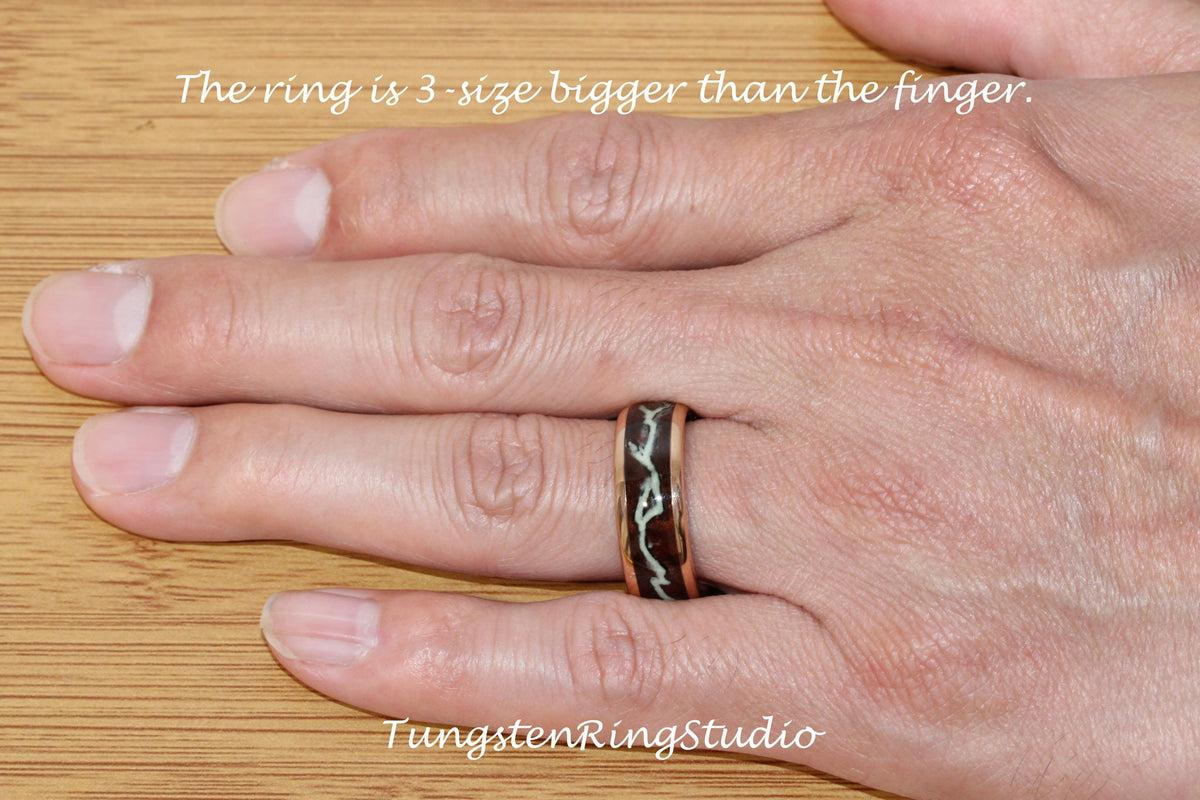 May include: A close-up of a hand wearing a black and white tungsten ring with a copper band. The ring has a unique design with white lines on a black background. The text "The ring is 3-size bigger than the finger." is visible above the hand. The text "TungstenRingStudio" is visible below the hand.