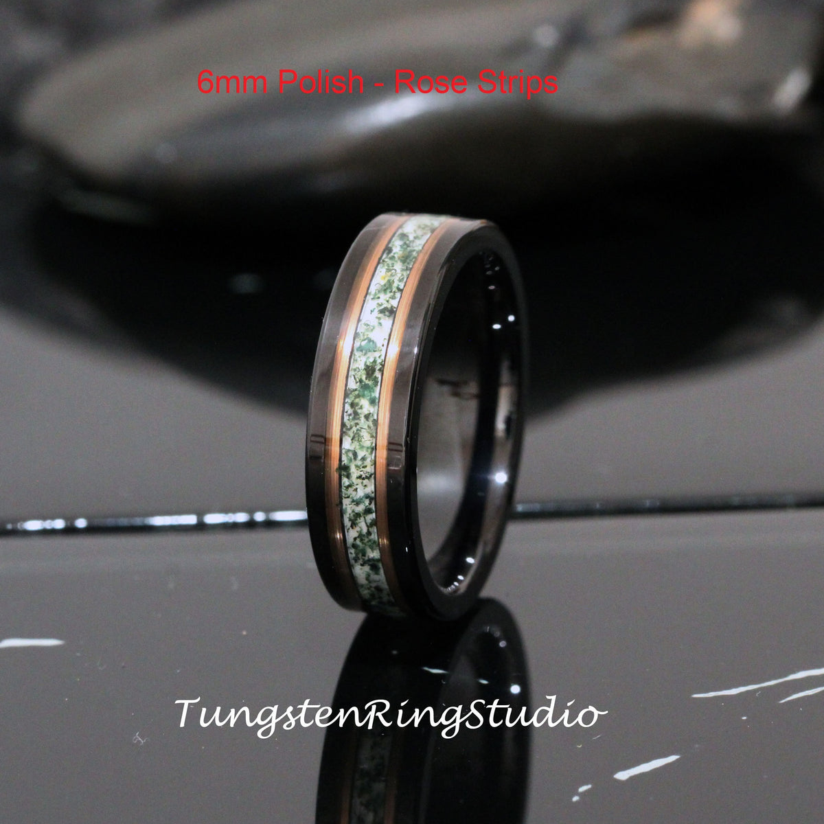 May include: A black tungsten ring with a rose gold inlay and green stone accents. The ring is 6mm wide and has a polished finish. The text "6mm Polish - Rose Strips" is visible in the image.