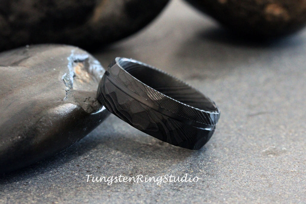 May include: A black tungsten carbide ring with a brushed finish and a diamond pattern. The ring is on a gray background.