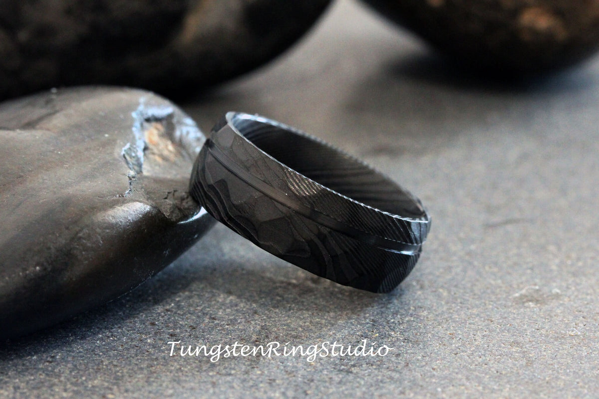 May include: A black tungsten carbide ring with a brushed finish and a diamond pattern. The ring is on a gray background.