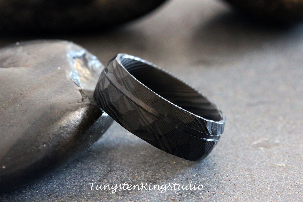May include: A black tungsten carbide ring with a brushed finish and a grooved edge. The ring is on a gray surface.