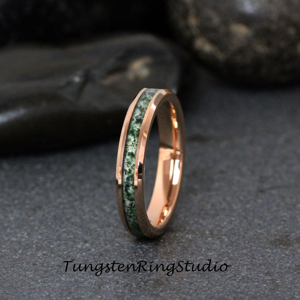 May include: A rose gold tungsten carbide ring with a green and white inlay. The ring is a simple band with a beveled edge.