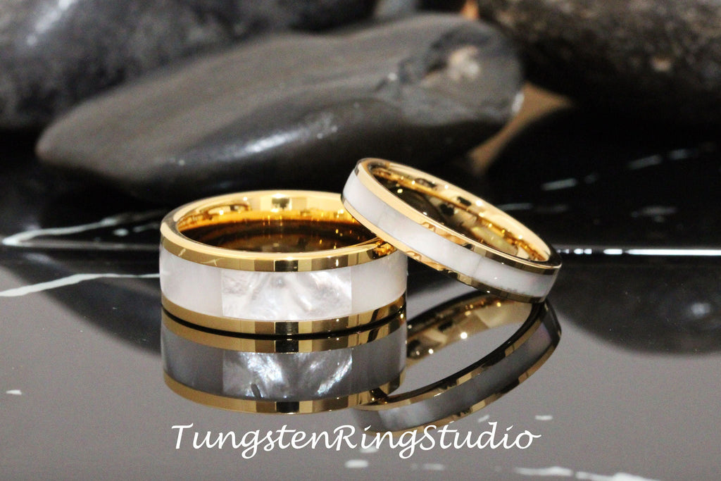 May include: Two gold tungsten carbide wedding bands with a white mother of pearl inlay. The bands are stacked on top of each other. TungstenRingStudio.