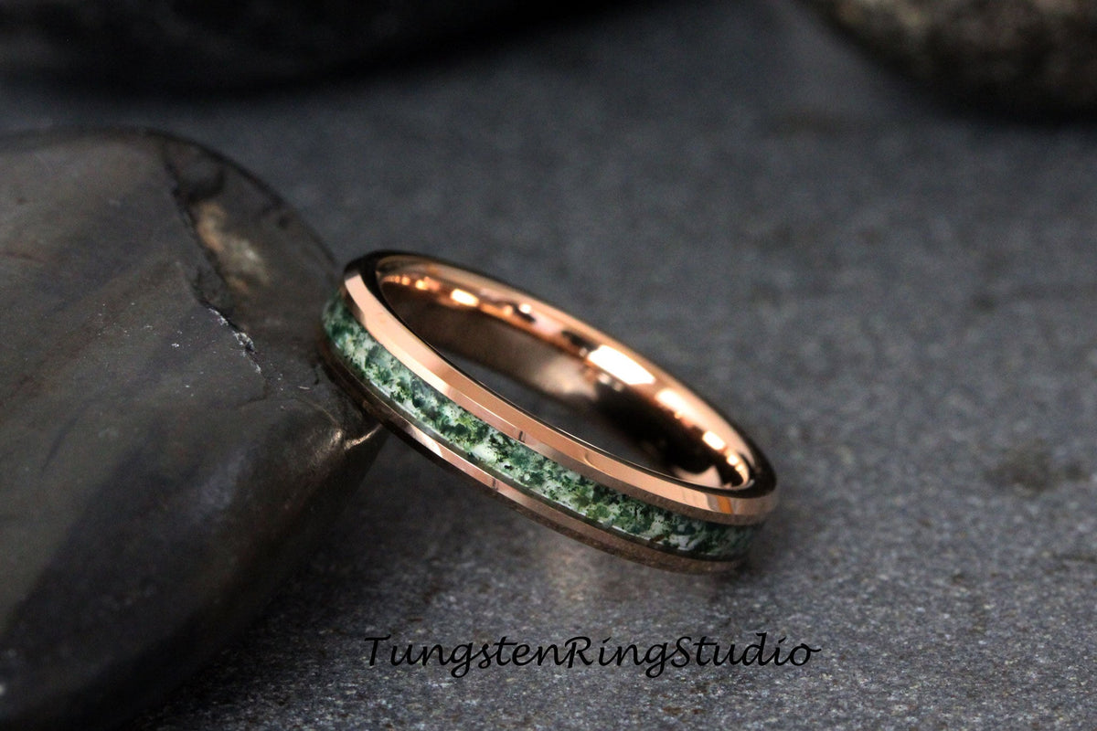 May include: A rose gold tungsten carbide ring with a green inlay. The ring has a beveled edge and a polished finish.