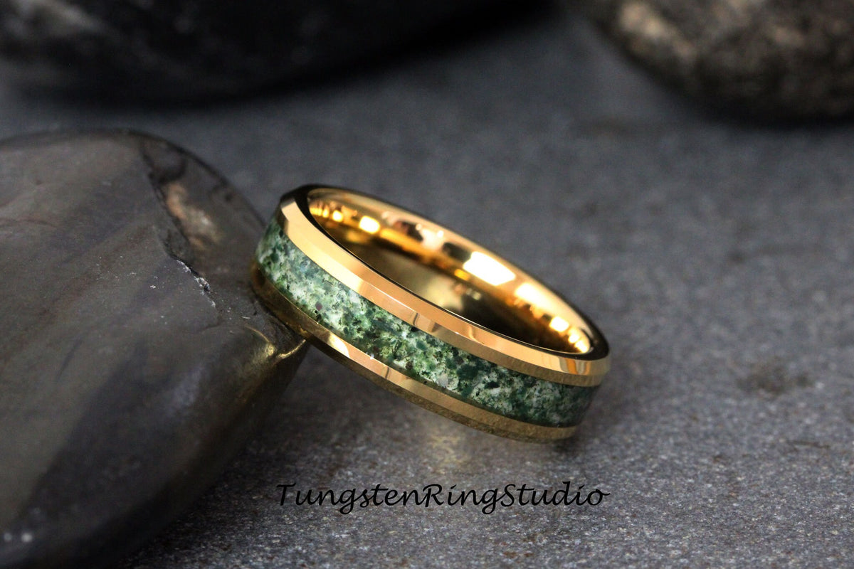 May include: A gold tungsten carbide ring with a green stone inlay. The ring has a beveled edge and a polished finish.