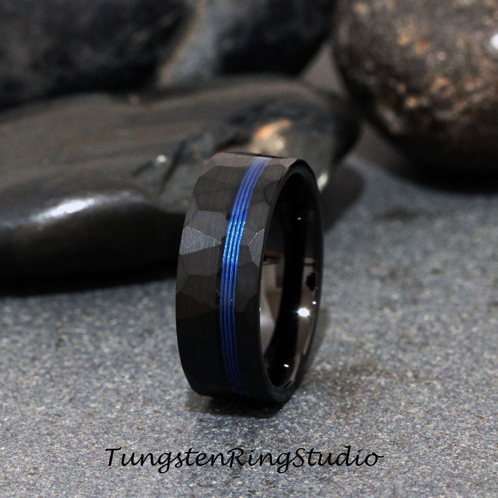 May include: A black tungsten carbide ring with a hammered finish and a blue line inlay. Tungsten Ring Studio.