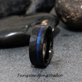 May include: A black tungsten carbide ring with a hammered finish and a blue line inlay. Tungsten Ring Studio.