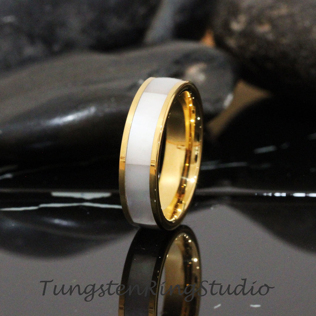May include: A gold and white tungsten carbide ring with a white inlay. The ring is polished and has a beveled edge.