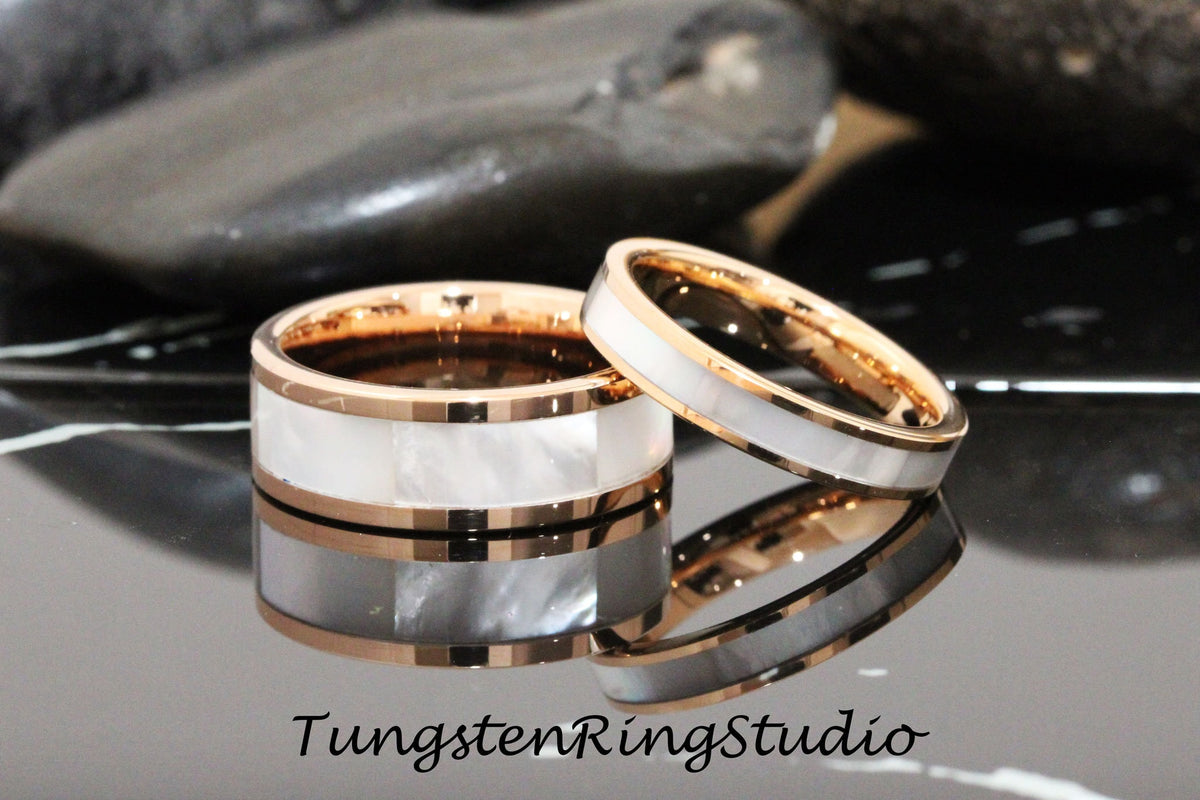 May include: Two tungsten carbide wedding bands with a rose gold inlay and a white mother of pearl inlay. The bands are stacked on top of each other.