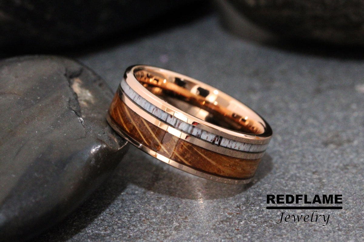 May include: A rose gold tungsten carbide ring with a brown wood inlay and white antler accents.  REDFLAME Jewelry.