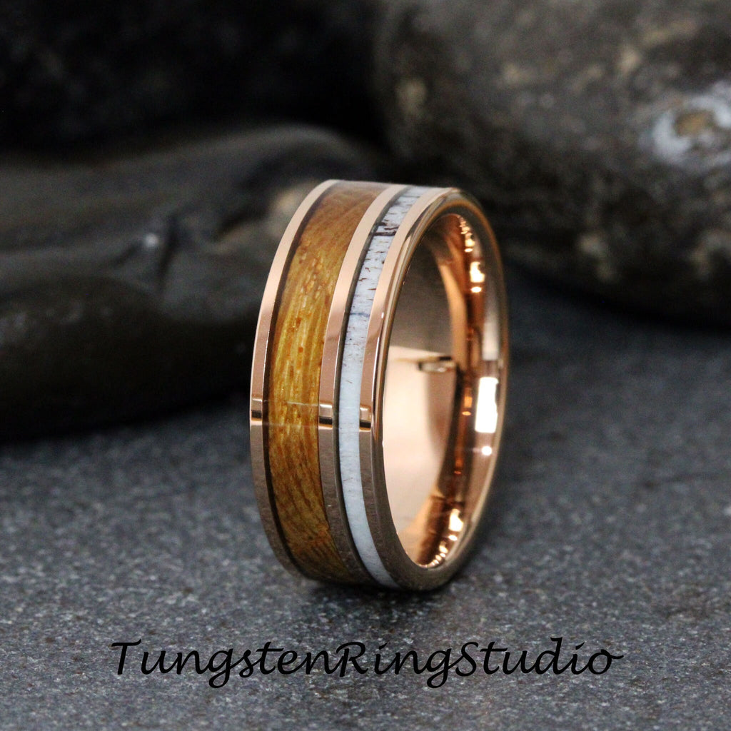May include: A rose gold tungsten carbide ring with a brown wood inlay and white antler accents. Tungsten Ring Studio.