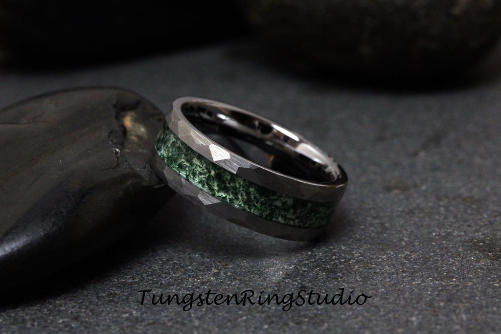 May include: A close-up of a tungsten ring with a hammered finish and a green stone inlay. The ring is silver-colored and sits on a dark, textured surface. The text "TungstenRingStudio" is visible.