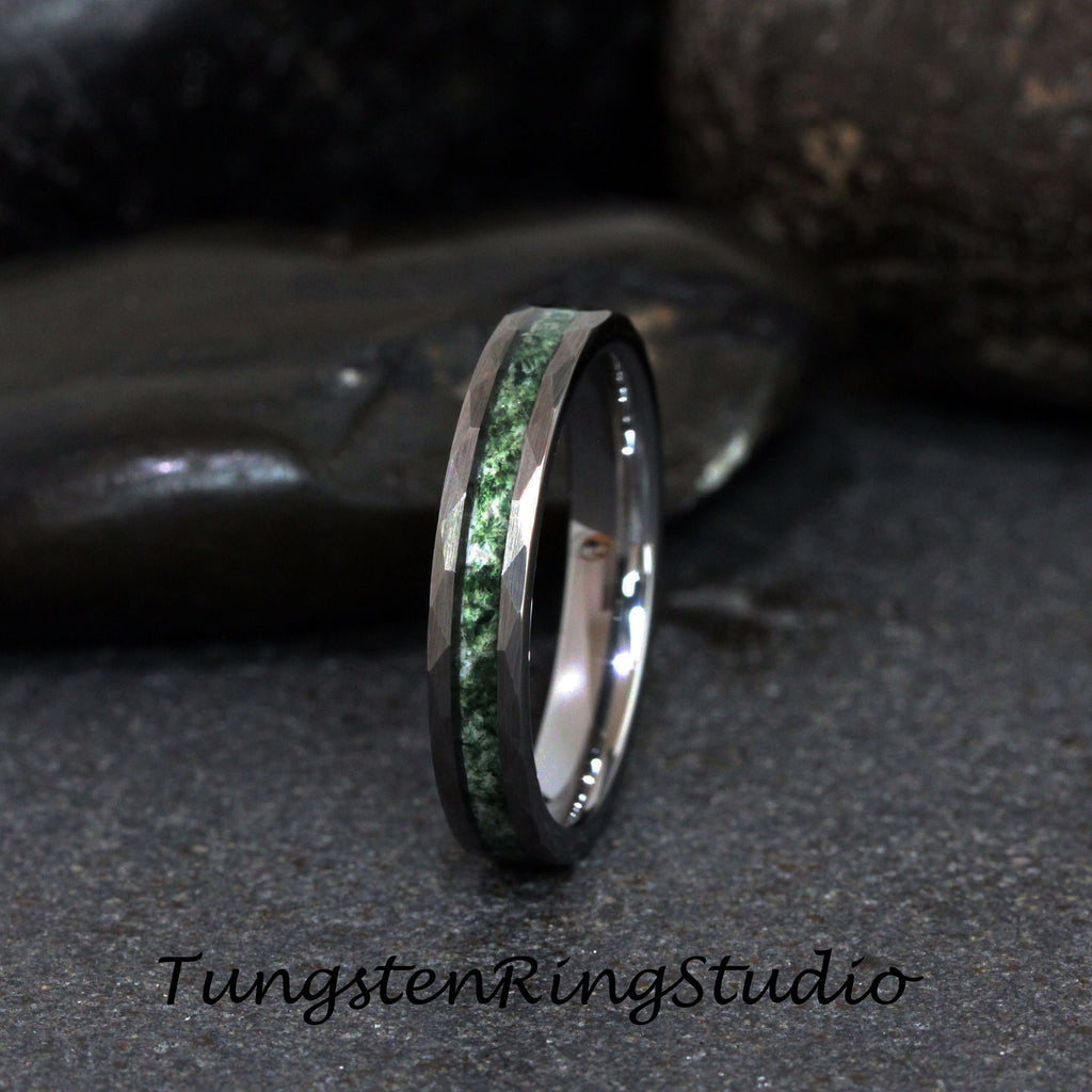 May include: A tungsten ring with a faceted, dark gray band and a central inlay of green stone. The ring is set against a dark gray background. The text "TungstenRingStudio" is at the bottom.