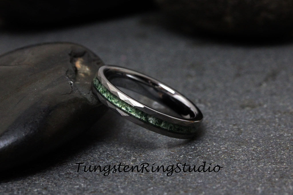 May include: A black tungsten ring with a green inlay. The ring has a beveled edge and is set on a gray background.