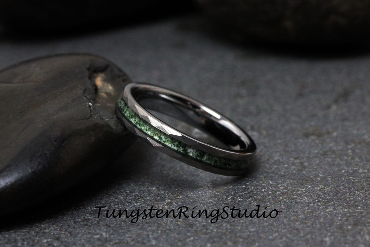 May include: A black tungsten ring with a green inlay. The ring has a beveled edge and is set on a gray background.