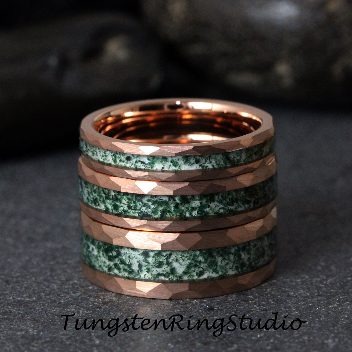 May include: Stack of rose gold rings with faceted edges, alternating with bands of green and white speckled stone. The rings are stacked on a dark surface. The text "TungstenRingStudio" is at the bottom.