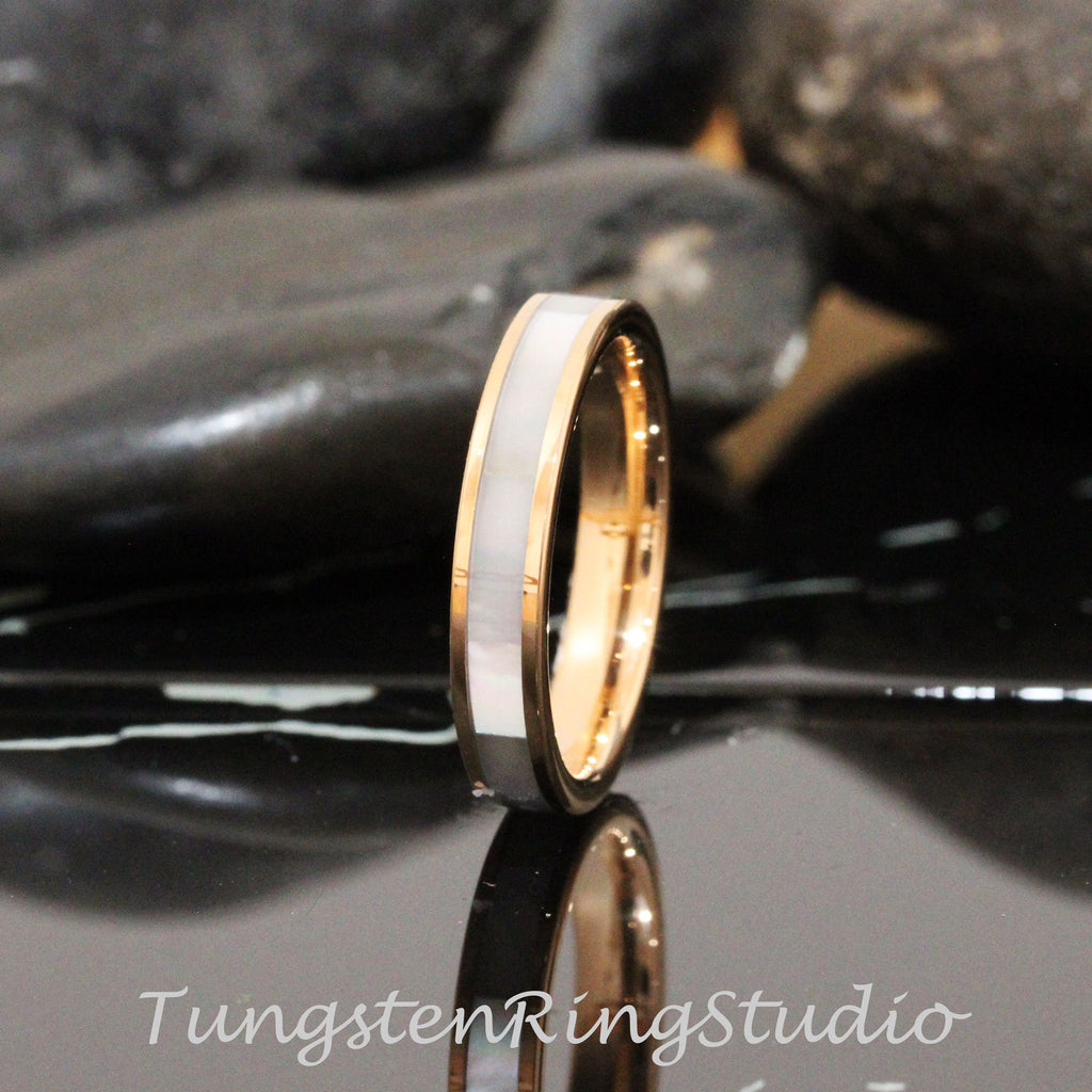 May include: A rose gold tungsten carbide ring with a white mother of pearl inlay. The ring is polished and has a beveled edge.