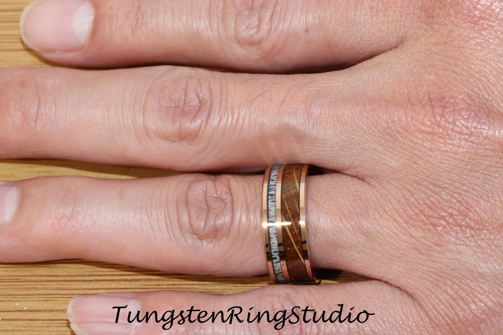 May include: A rose gold tungsten ring with a brown wood inlay and white accents. The ring is worn on a person's finger.