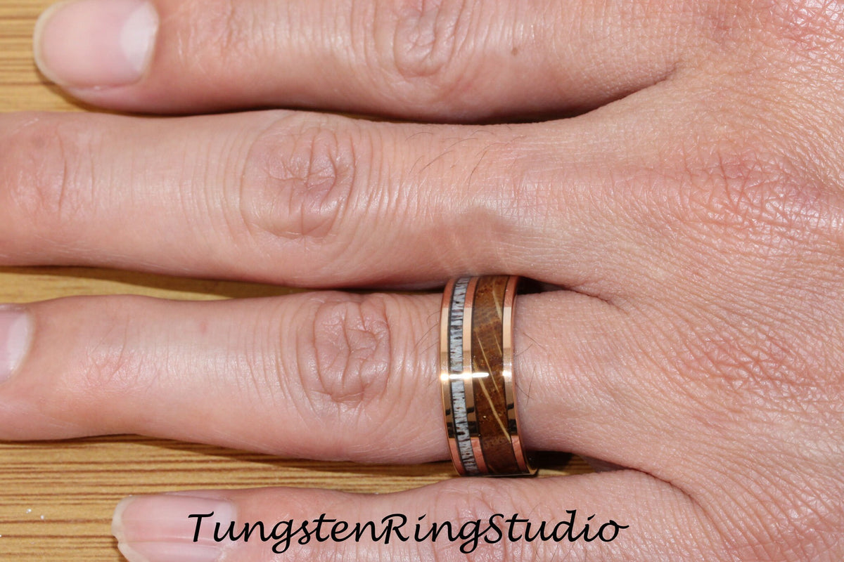 May include: A rose gold tungsten ring with a brown wood inlay and white accents. The ring is worn on a person's finger.