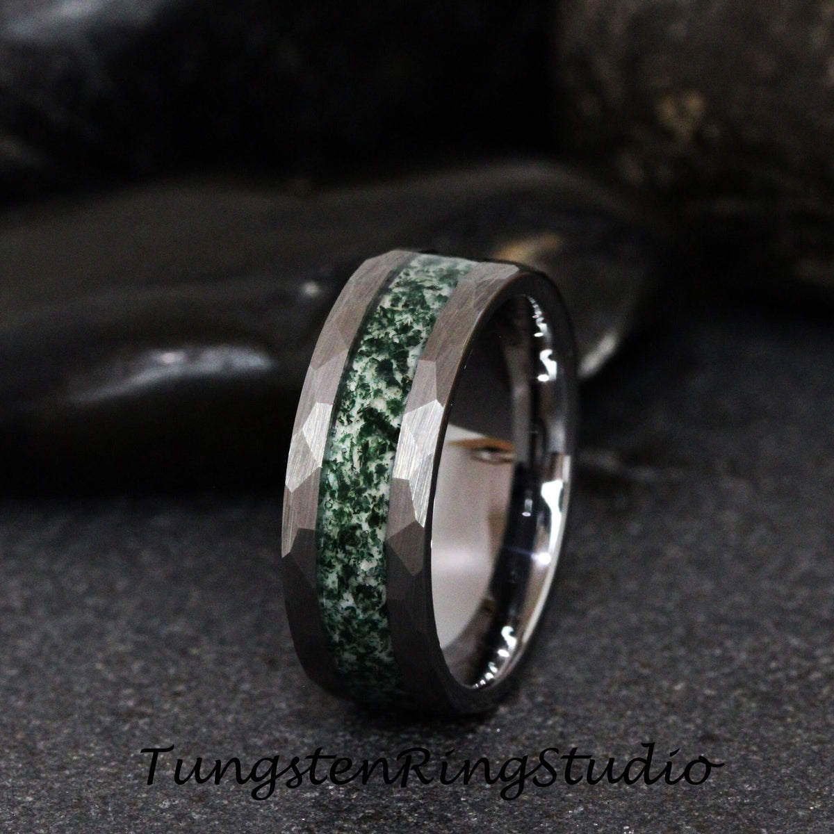May include: A tungsten ring with a hammered finish and a central inlay of green stone. The ring has a faceted design on the outer edges and a polished inner band. The text "TungstenRingStudio" is visible at the bottom.