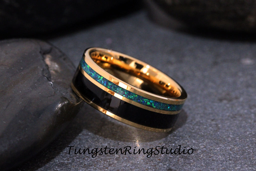 May include: A gold tungsten carbide ring with a black inlay and a green opal inlay. The ring is on a dark gray background.