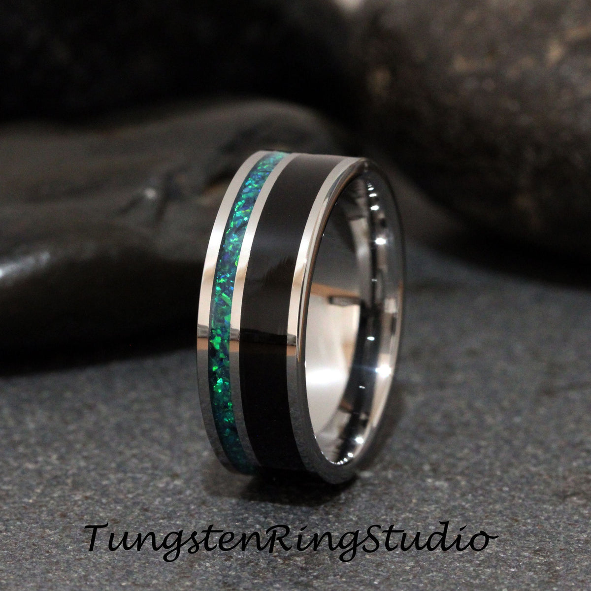 May include: A silver tungsten carbide ring with a black inlay and a green opal inlay. The ring is a wedding band.