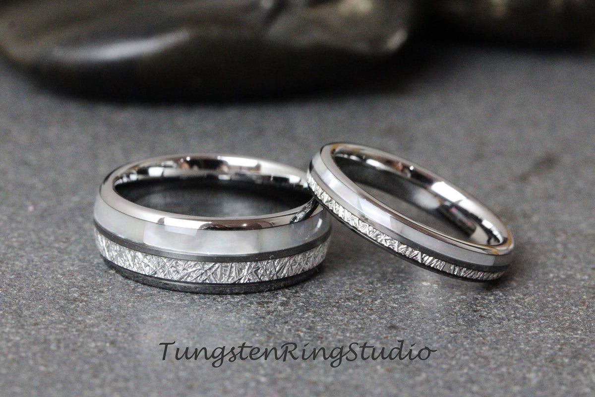 May include: Two matching wedding rings. The rings have a silver band with a white inlay and a textured, dark gray band. The rings are on a gray surface. The text "TungstenRingStudio" is at the bottom.