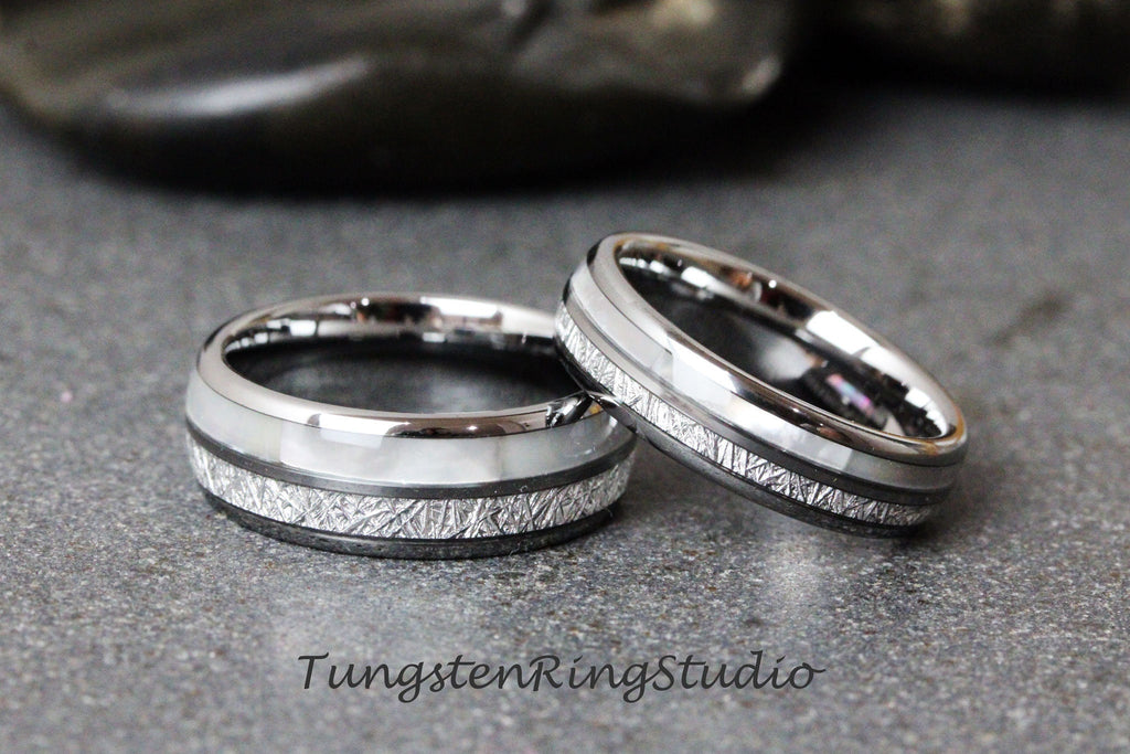 May include: Two silver tungsten carbide wedding bands with a white inlay and a textured finish. The bands are stacked on top of each other.