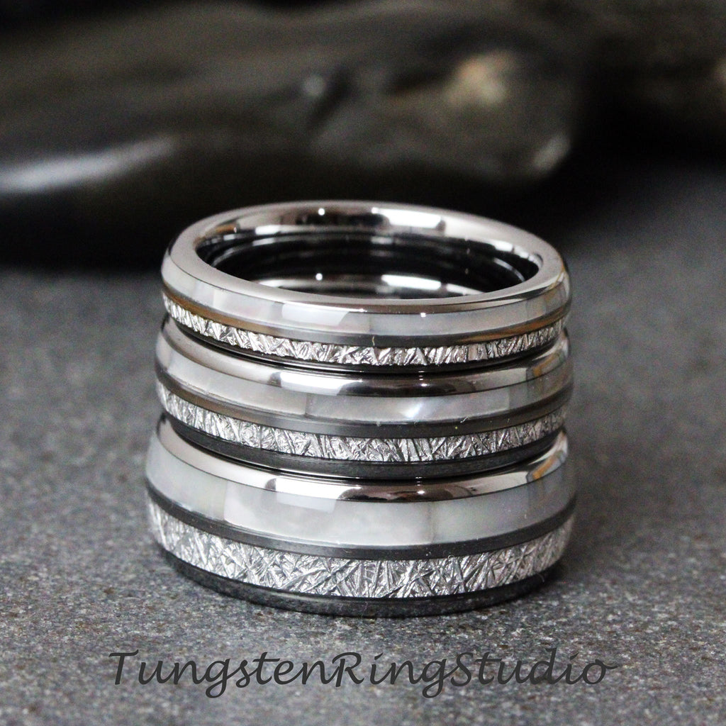 May include: Stack of four silver tungsten carbide rings with a white inlay and a brushed finish. Each ring has a different pattern of lines etched into the surface.