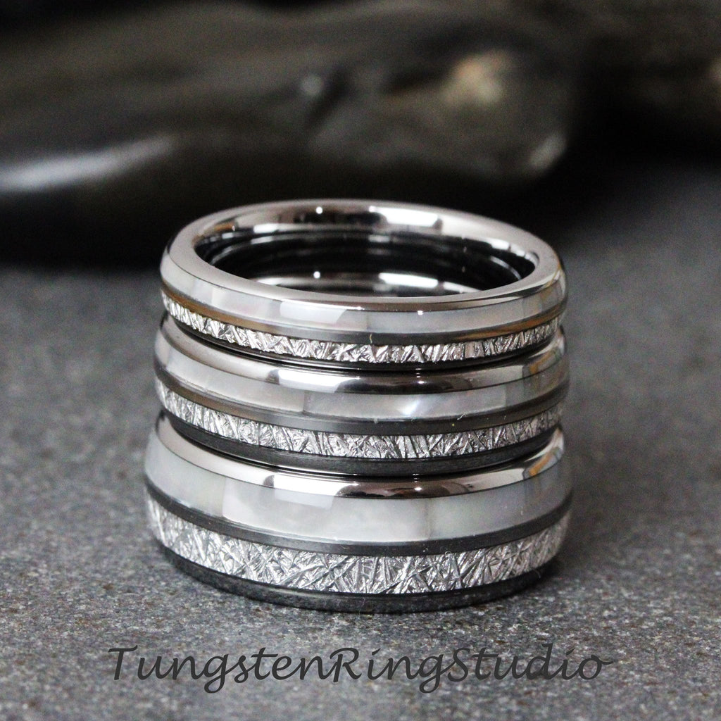 May include: Stack of four silver tungsten carbide rings with a white inlay and a brushed finish. Each ring has a different pattern of lines etched into the surface.
