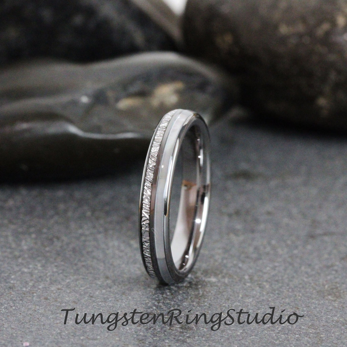May include: A silver tungsten carbide ring with a white inlay and a textured band. Tungsten Ring Studio.