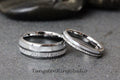 May include: Two silver tungsten wedding bands with a white inlay and a textured finish. The bands are on a gray surface. TungstenRingStudio.