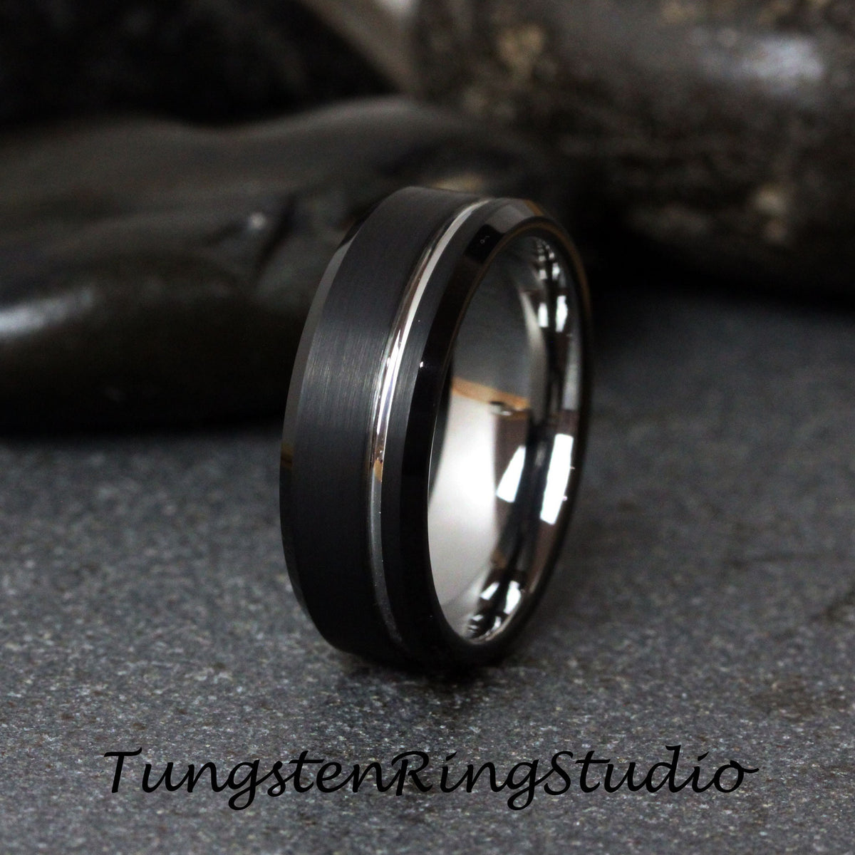 May include: A black tungsten carbide ring with a polished silver band. The ring has a beveled edge and a brushed finish.