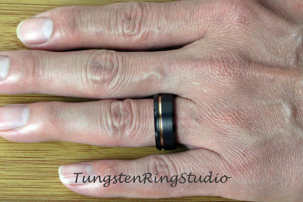 May include: A black tungsten ring with a gold inlay and a brushed finish. The ring is worn on a person's finger.