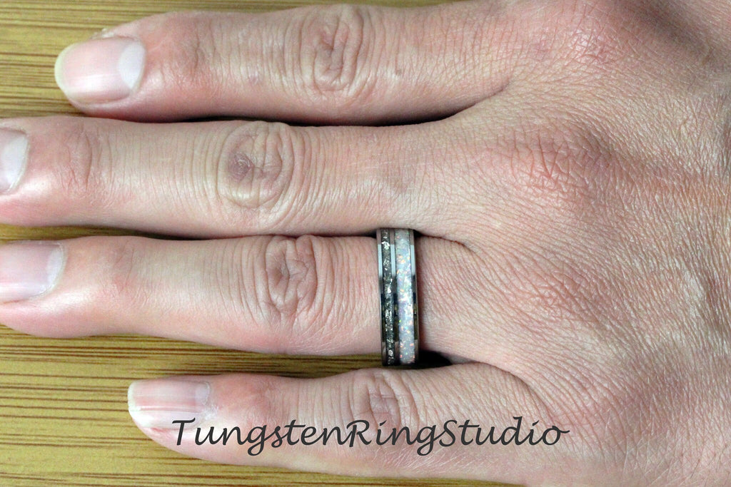 May include: A silver tungsten carbide ring with a white opal inlay. The ring is on a person's finger.