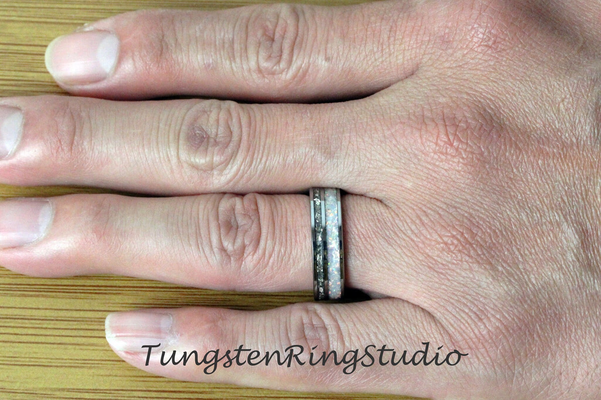 May include: A silver tungsten carbide ring with a white opal inlay. The ring is on a person's finger.