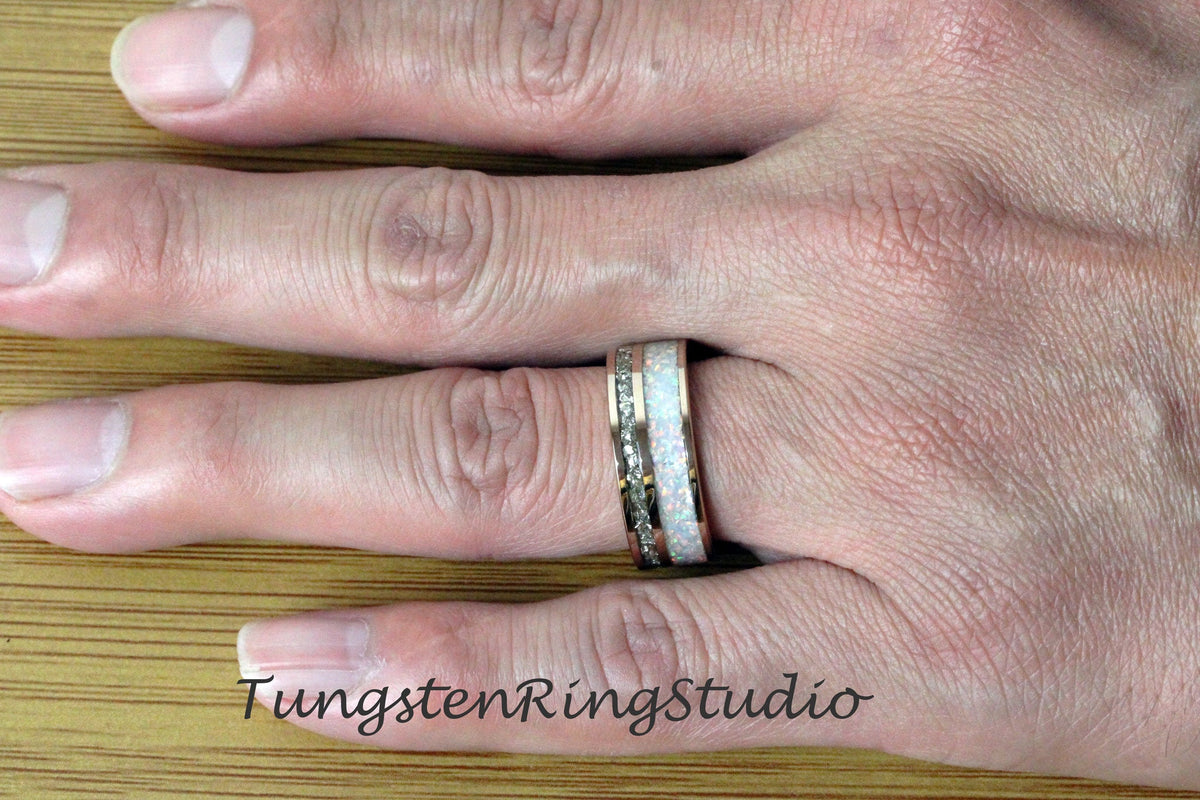 May include: A silver tungsten carbide ring with a white opal inlay. The ring is on a person's finger.