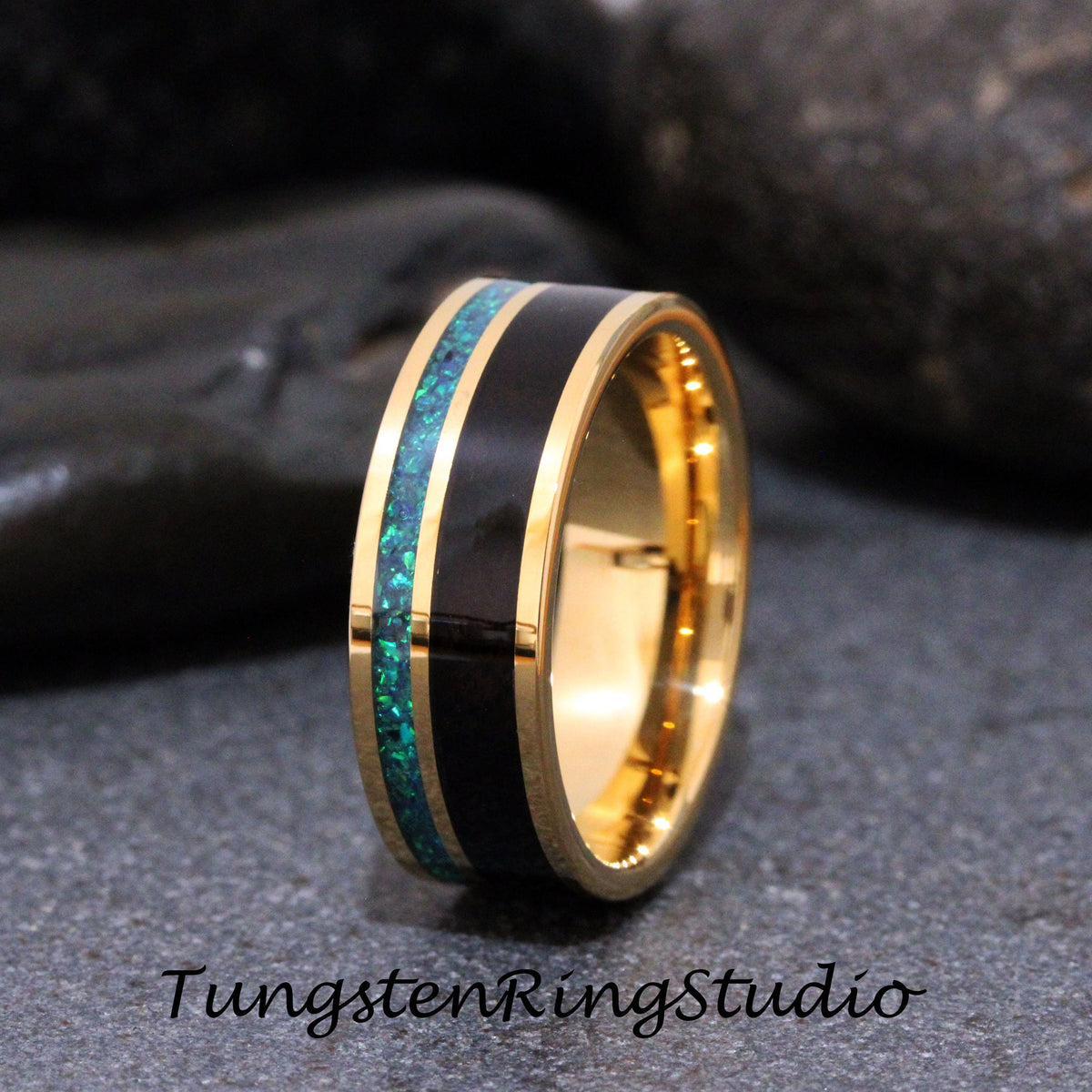 May include: A gold tungsten carbide ring with a black inlay and a green opal inlay. Tungsten Ring Studio.