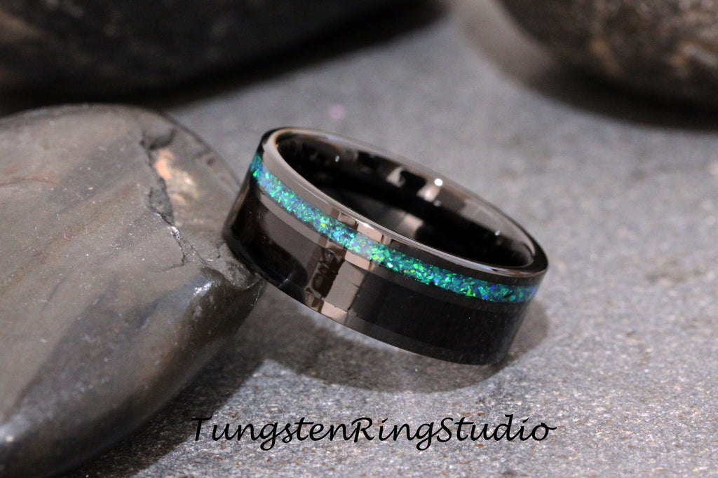 May include: A black tungsten ring with a thin green opal inlay. The ring is on a gray stone surface.